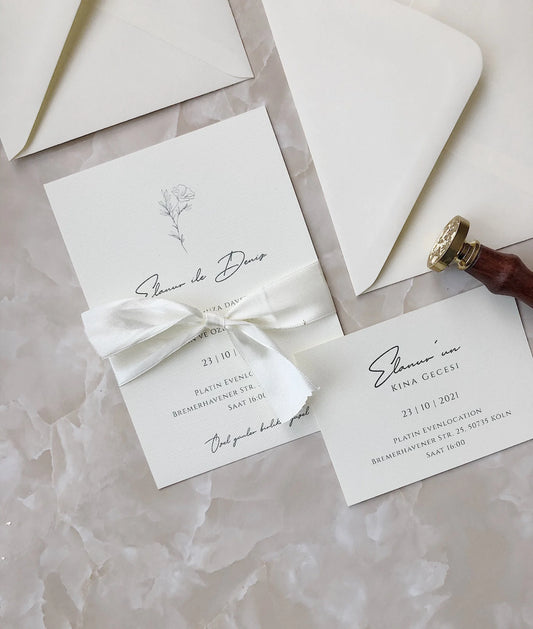 Elegante Hochzeitseinladung aus cremefarbenem Karton mit Schleife und Blumendruck auf Marmor-Hintergrund