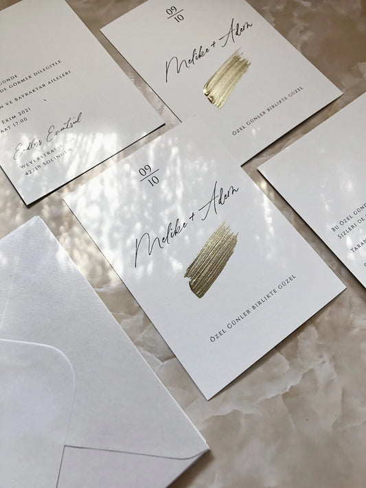 Moderne Hochzeitseinladung mit Goldakzent auf weißem Papier, Umschlag im Hintergrund