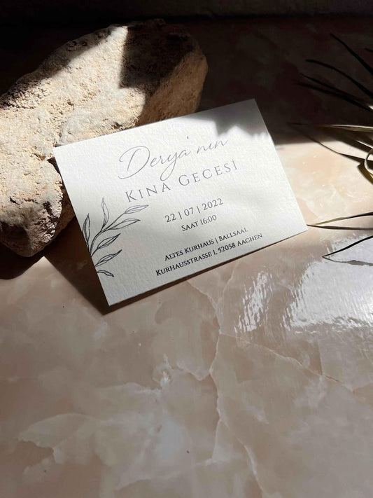 Elegante Hochzeitseinladung aus Büttenpapier mit Eukalyptus Motiv auf Marmortisch, Sonnenlicht