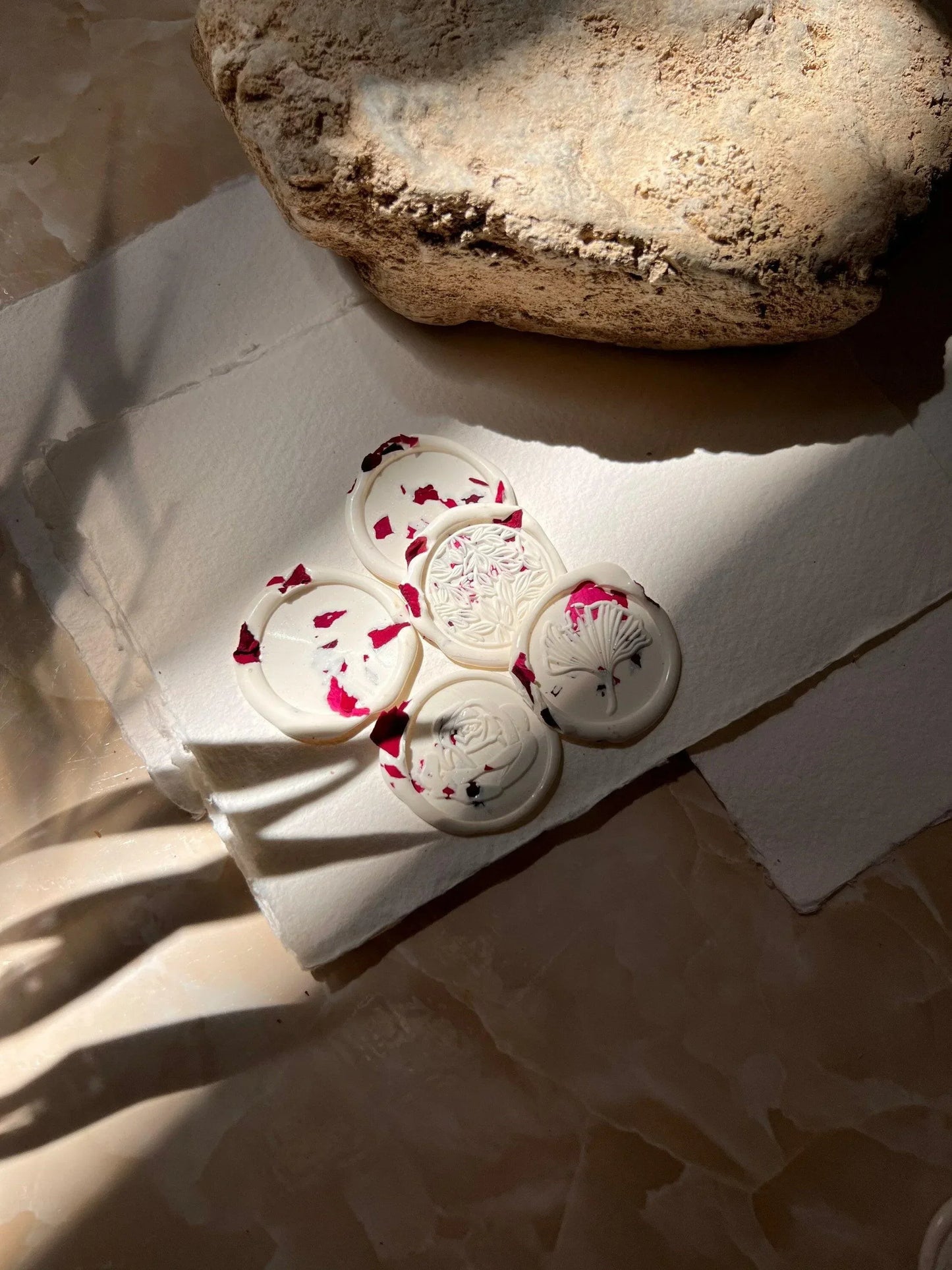 Handgemachte weiße Wachssiegel mit Blumenmuster und roten Blütenblättern auf Büttenpapier
